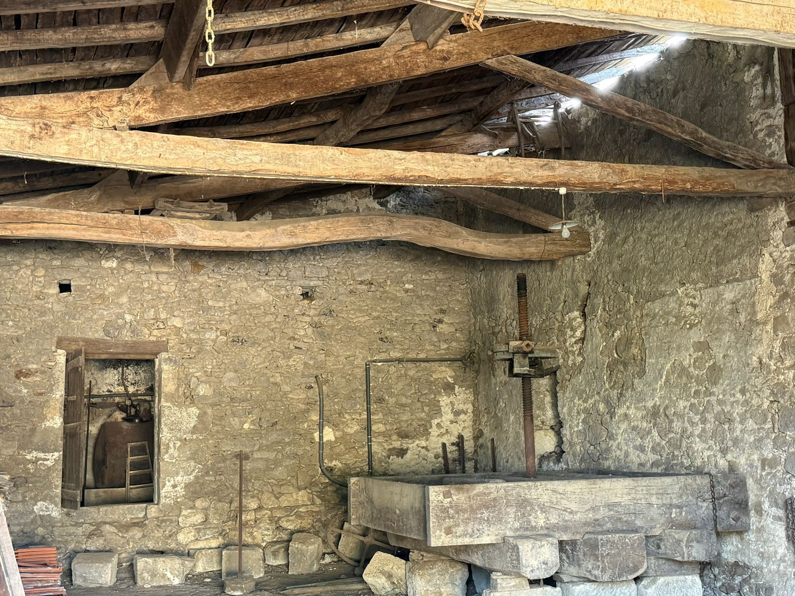 Old press inside the stone barn beneath exposed timber roof beams