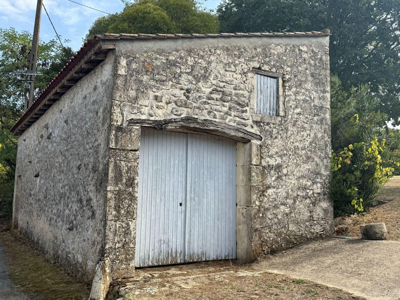 Small stone garage with a closed pale door and an upper opening